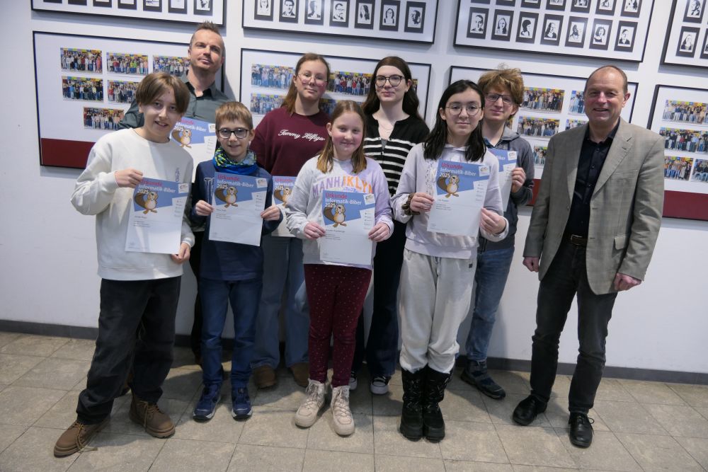 Das Foto zeigt einige der erfolgreichen Teilnehmerinnen und Teilnehmer am Informatik-Biber 2026 zusammen mit StR Thomas Engelhardt und Schulleiter Dr. Thomas Pauer.